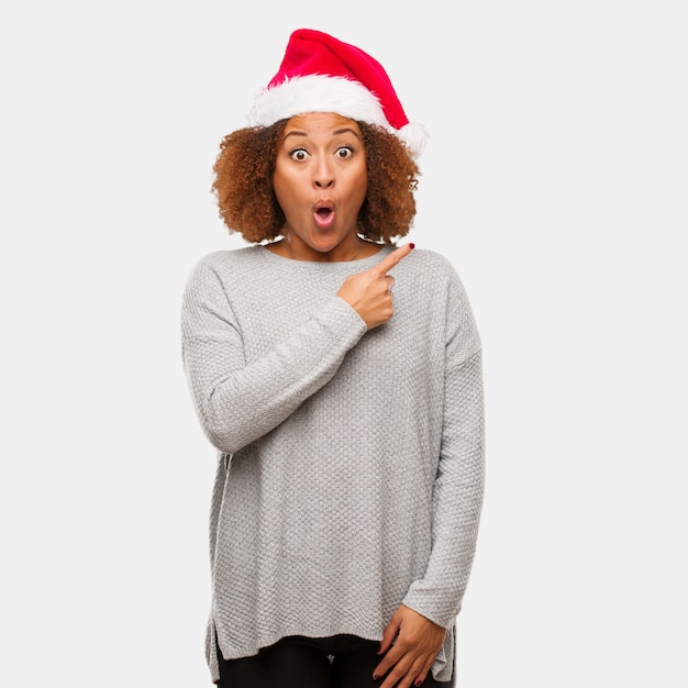 Young black woman wearing a santa hat pointing to the side