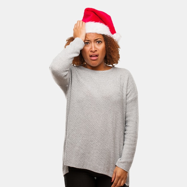 Young black woman wearing a santa hat worried and overwhelmed