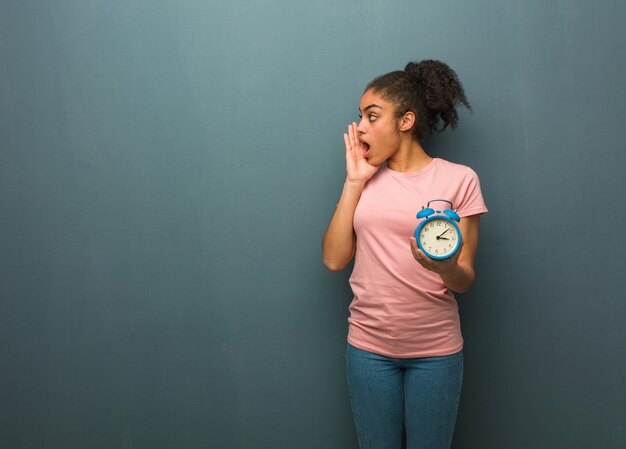 Young black woman whispering gossip undertone. She is holding an alarm clock.