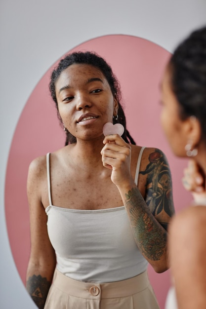 Young black woman with acne scars using face massager during beauty routine