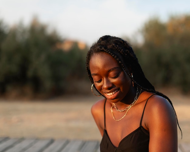 A young black woman with braids in her hair relaxes and rests during a walk at sunset