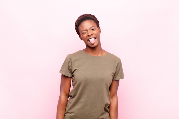 Young black womanlooking goofy and funny with a silly cross-eyed expression, joking and fooling around on pink wall