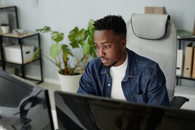 young blackman in casual clothes sitting in front of computer monitors
