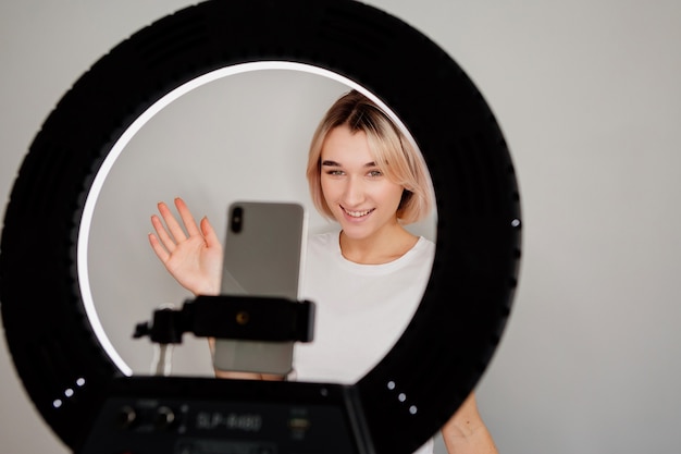 Young blogger girl is broadcasting live online at home with a ring lamp and a smartphone