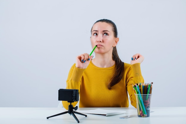 Young blogger girl is thinking by holding pencil on lips on white background