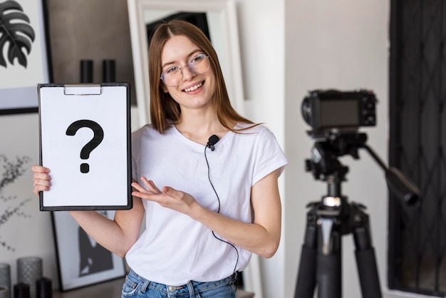 Young blogger recording with professional camera holding clipboard with question mark