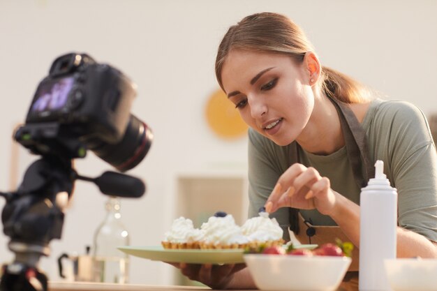 Young blogger showing the process of decorating the baked cakes and shooting it on the video