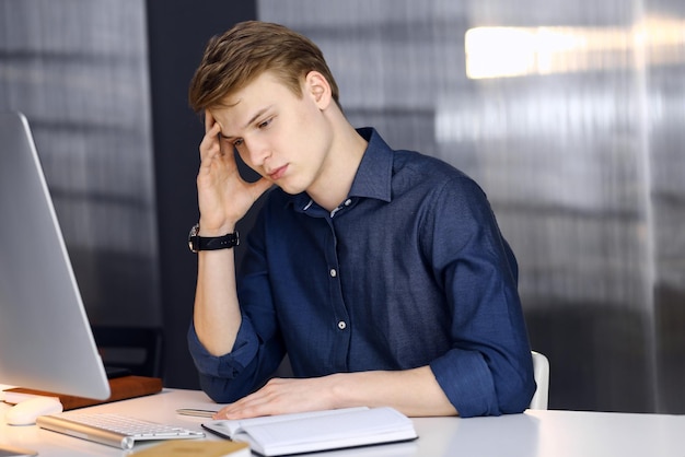 Young blond businessman feeling stress at workplace in office. Startup business means working hard and out of time for success achievement.