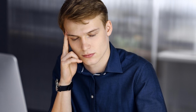 Young blond businessman feeling stress at workplace in office. Startup business means working hard and out of time for success achievement.