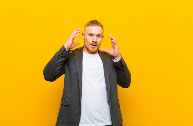 Young blond businessman screaming with hands up in the air, feeling furious, frustrated, stressed and upset