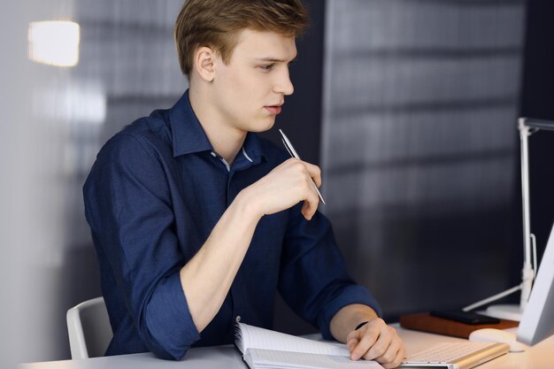 Young blond businessman thinking about strategy at his working\
place with computer. startup business means working hard and out of\
time for success achievement.