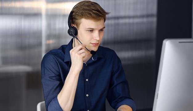 Young blond businessman using headset and computer at work. Startup business means working hard and out of time for success achievement.