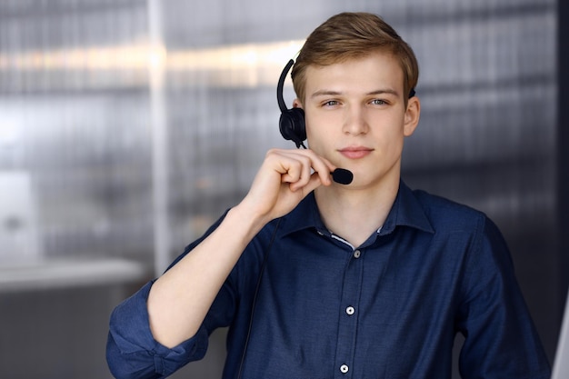 Young blond businessman using headset and computer at work. Startup business means working hard and out of time for success achievement.