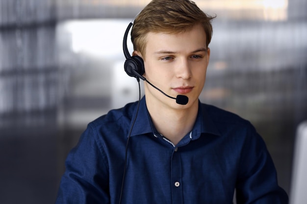 Young blond businessman using headset and computer at work. Startup business means working hard and out of time for success achievement.