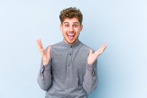 Young blond curly hair caucasian man isolated celebrating a victory or success, he is surprised and shocked.