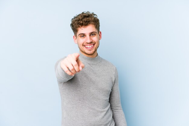 Young blond curly hair caucasian man isolated cheerful smiles pointing to front.