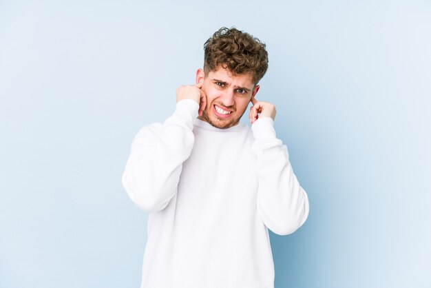 Young blond curly hair caucasian man isolated covering ears with hands