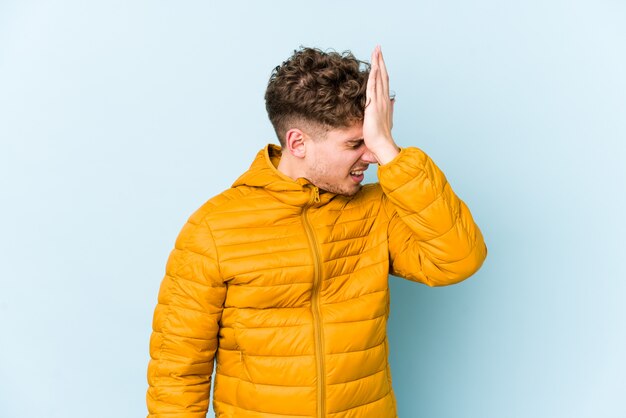 Young blond curly hair caucasian man isolated forgetting something, slapping forehead with palm and closing eyes.