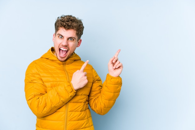 Young blond curly hair caucasian man isolated pointing with forefingers to a copy space, expressing excitement and desire.