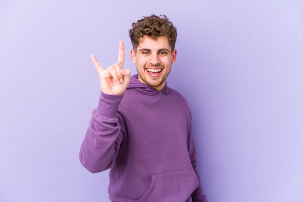 Photo young blond curly hair caucasian man isolated showing a horns gesture as a revolution concept.