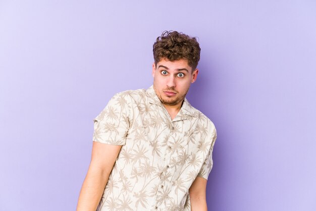 Young blond curly hair caucasian man isolated shrugs shoulders and open eyes confused.