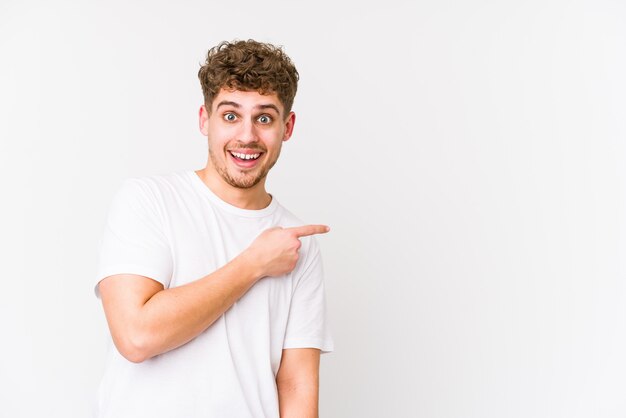 Young blond curly hair caucasian man isolated smiling and pointing aside, showing something at blank space.