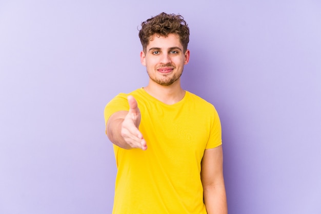 Il giovane uomo caucasico dei capelli ricci biondi ha isolato la mano d'allungamento alla macchina fotografica nel gesto di saluto.