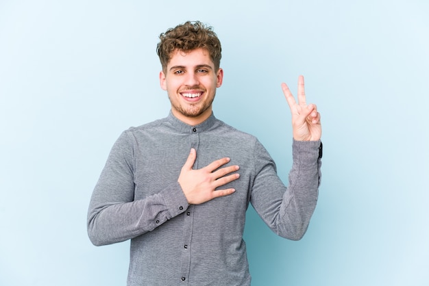 Young blond curly hair caucasian man isolated taking an oath, putting hand on chest.