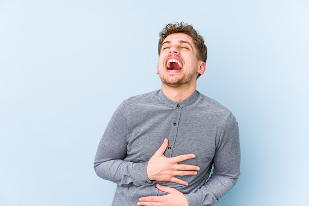 Young blond curly hair caucasian man laughs happily and has fun keeping hands on stomach.