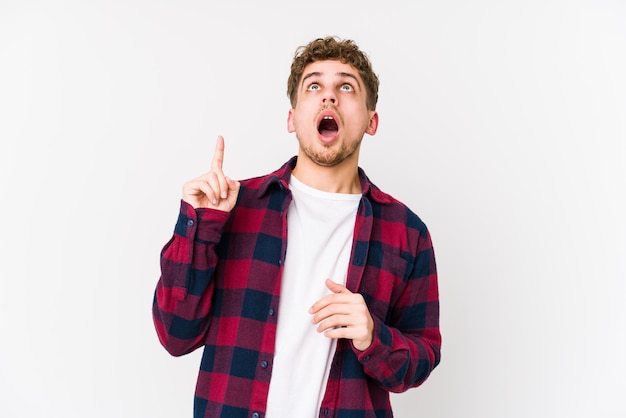 Young blond curly hair caucasian man pointing upside with open mouth.