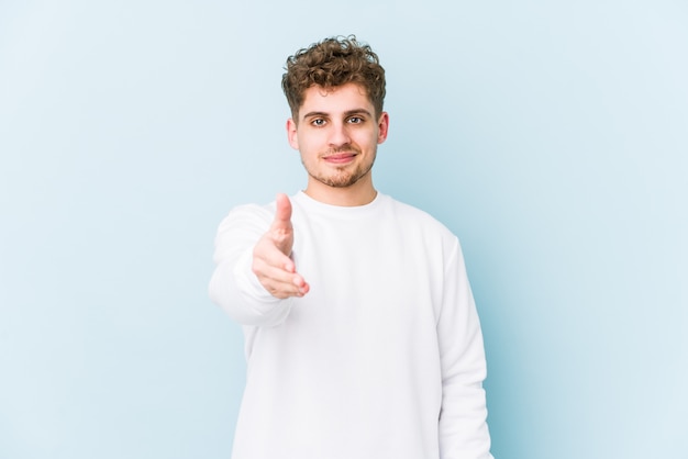 Young blond curly hair man stretching hand at camera in greeting gesture.