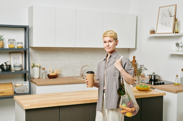 Young blond female holding a bag on shoulder and drink in hand