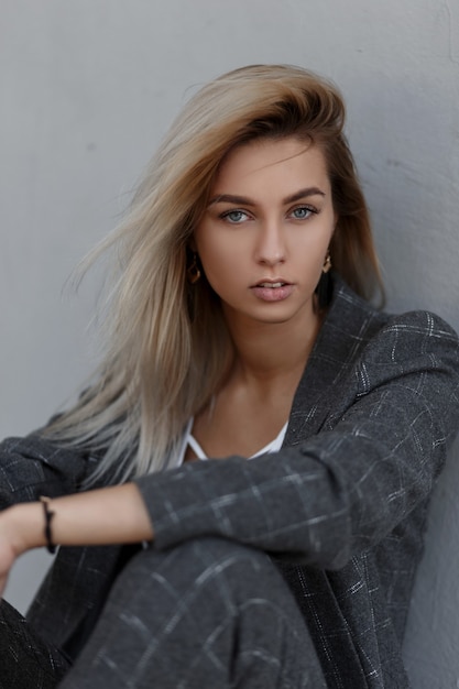 Young blond girl in a fashionable vintage suit sitting near a gray wall in the street