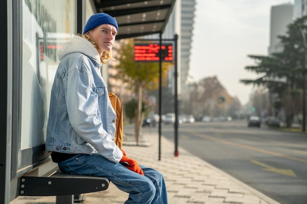 Photo young blond guy student waiting transport very long time in morning man on bus stop