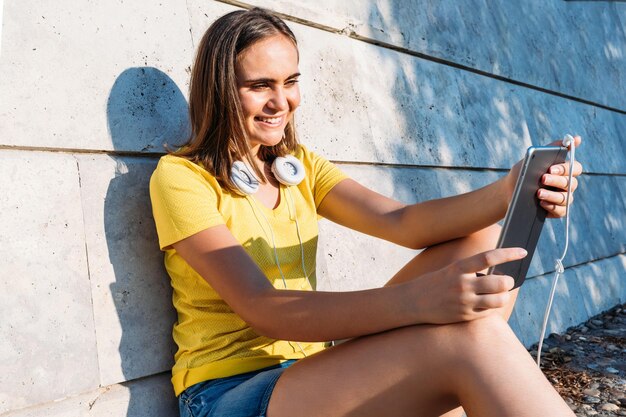 Young blond hair girl wearing yellow t-shirt and white headphones, smiling and looking at her tablet. Technology, lifestyle and relaxation concept