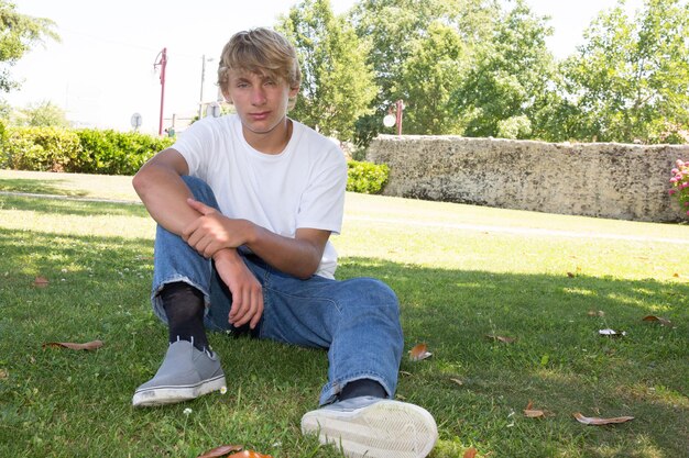 Young blond man sit on grass summer