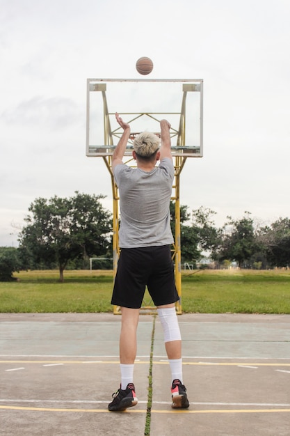 Young blond man throwing a ball on an abandoned basketball\
court.