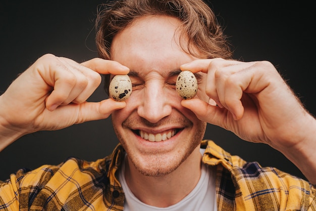 Young blond man in yellow shirt is covering eyes up with quail eggs