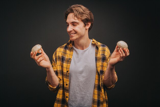 Young blond man in yellow shirt is holding mushrooms in both hands