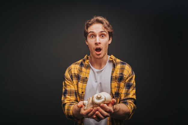 Young blond man in yellow shirt is holding mushrooms in hands with surprise