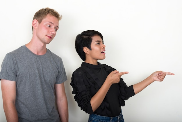 young blond man and young Asian woman as multi ethnic couple together against white wall