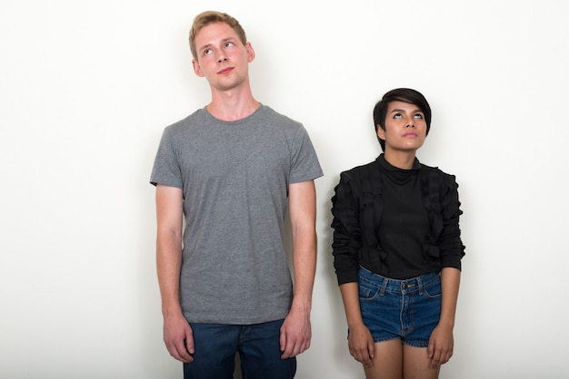 young blond man and young Asian woman as multi ethnic couple together against white wall