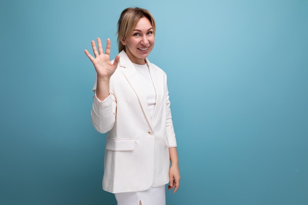 Young blond manager woman in a white elegant jacket and skirt greets with a hand gesture