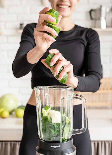 Young blond smiling woman making green smoothie at home kitchen