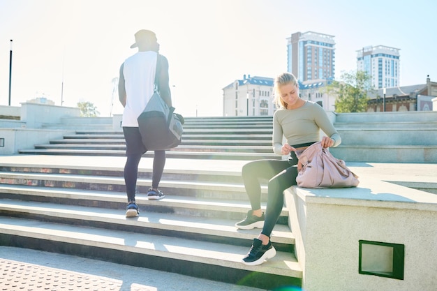 Young blond sportswoman sitting on concrete edge by staircase outdoors