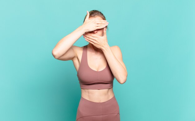 Young blond woman covering face with both hands