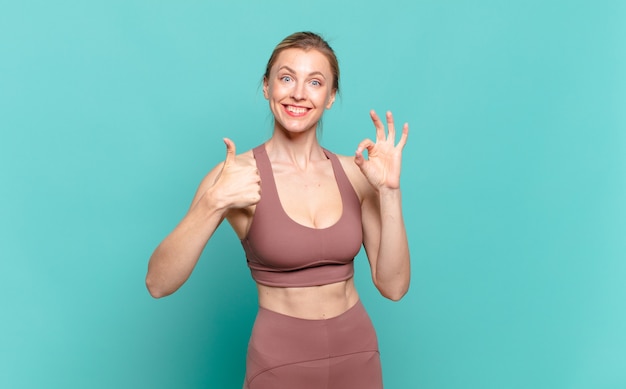 Young blond woman feeling happy, amazed, satisfied and surprised, showing okay and thumbs up gestures, smiling. sport concept