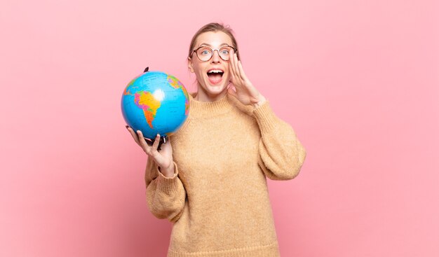 Foto giovane donna bionda che si sente felice, eccitata e positiva, emette un grande grido con le mani vicino alla bocca, chiamando. concetto di mondo