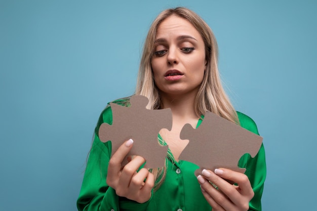 Young blond woman holding a puzzle in her hands on a blue background