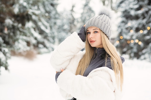 冬の森を歩いている白いコートを着た若いブロンドの女性。テキスト用のスペース